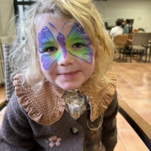 Niña pequeña con mariposa lila y verde en cara