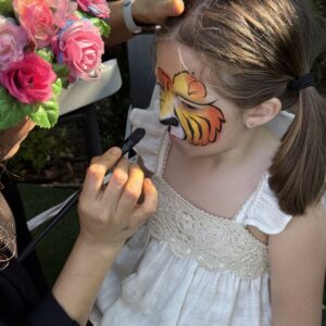 Niña con maquillaje de tigre siendo pintada por Lucy junto a flores