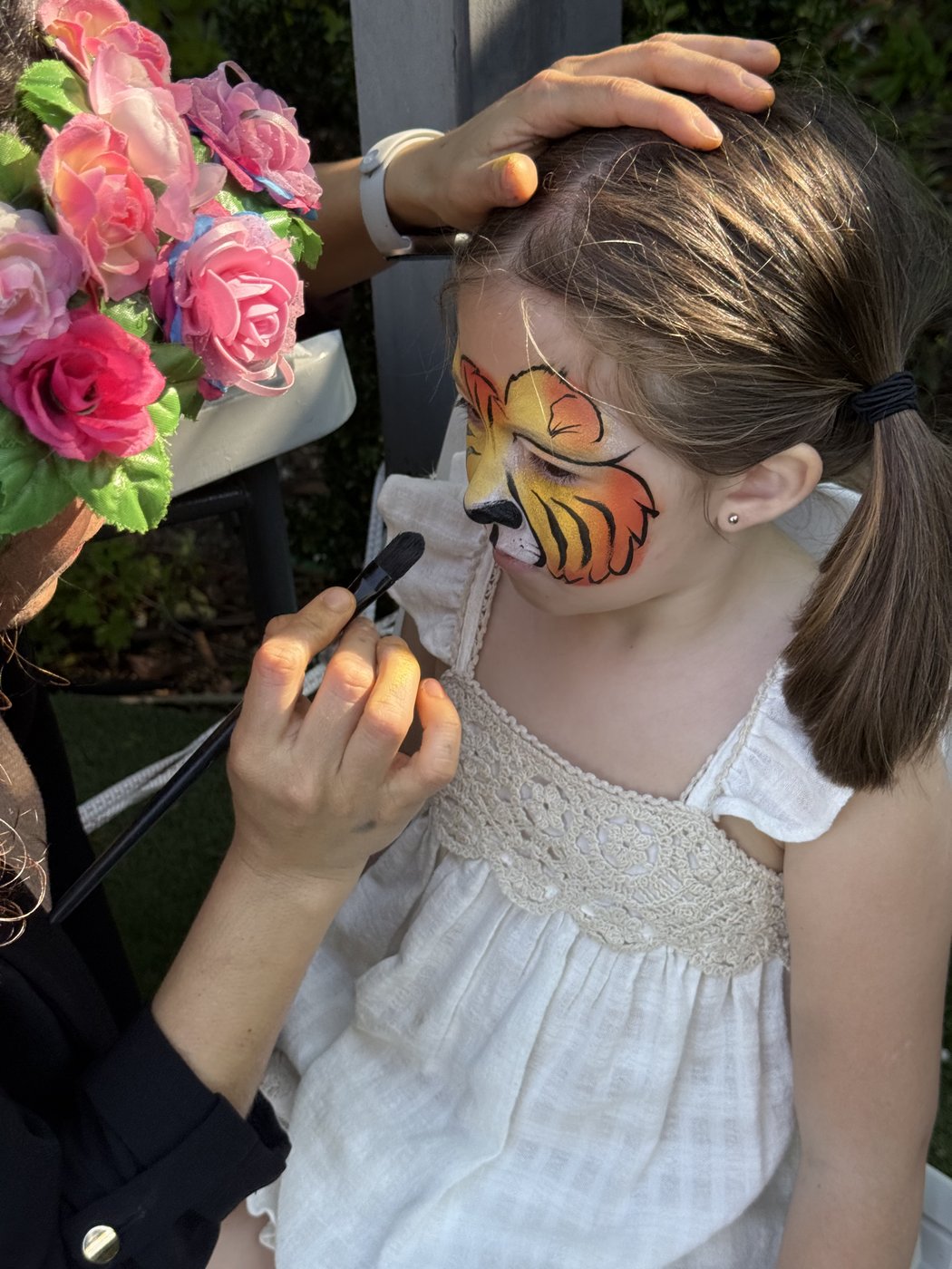 Niña con maquillaje de tigre siendo pintada por Lucy junto a flores